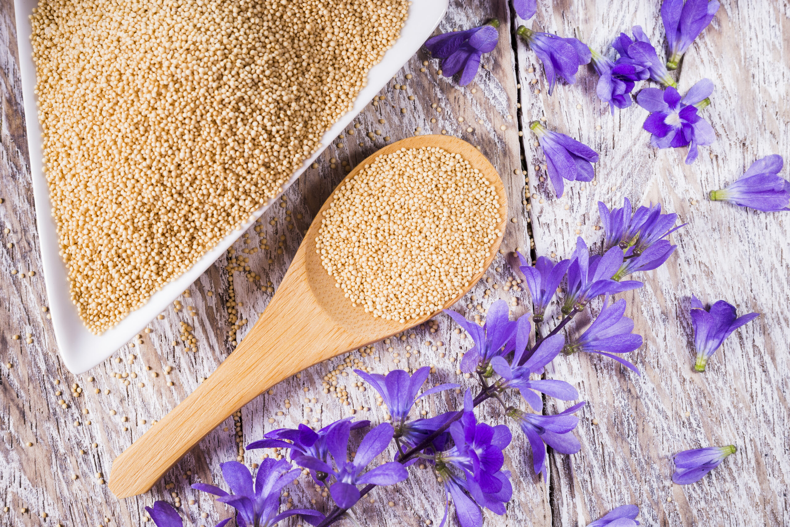 Bowl with amaranth grains on wooden background, top view
