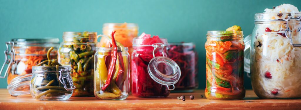 Assorted fermented vegetables in glass jars, including kimchi, pickled peppers, and other probiotic-rich foods.