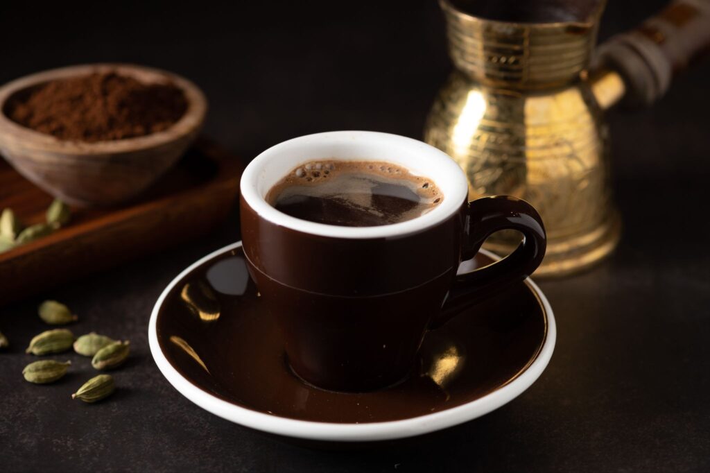 Cup of spiced coffee with cardamom pods and a traditional coffee pot.